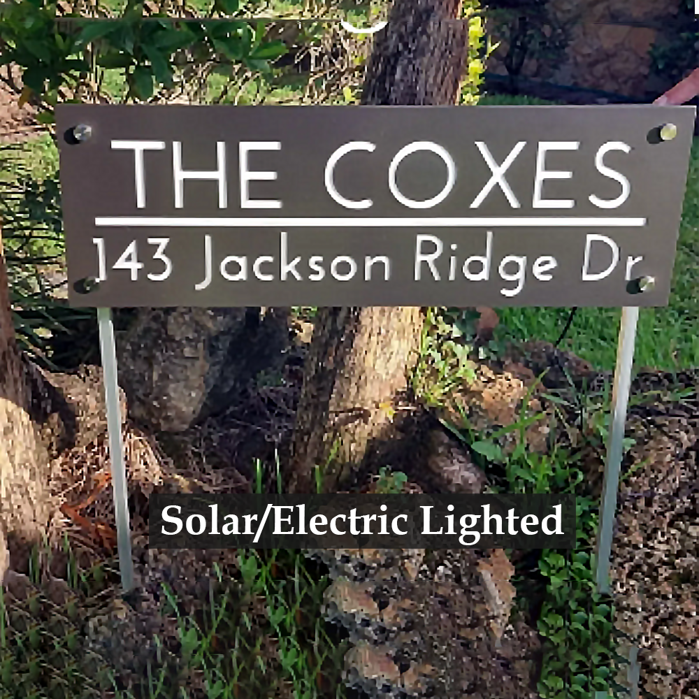 A decorative Lighted Family/Address Sign with Ground Stakes in various finishes, illuminated at night, powered by solar energy, and built to withstand outdoor conditions. Product features include laser-cut numbers and letters, commercial-grade aluminum and steel construction, a powder-coated finish, super bright LED lights with a large solar panel, day/night automatic illumination, fully sealed design, and easy visibility from over 70 feet away. 